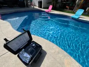 Grey Shark Pool Services, Oak Island, NC: poolside on a sunny day, test kit on concrete edge, three pool chairs float in clear water.