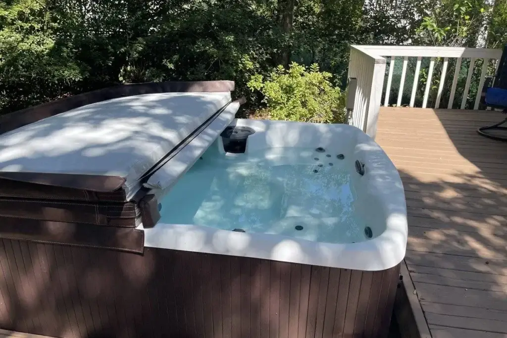 A hot tub serviced by Grey Shark Pool Services on a wooden deck in Oak Island, NC, with trees and sunlight casting shadows.