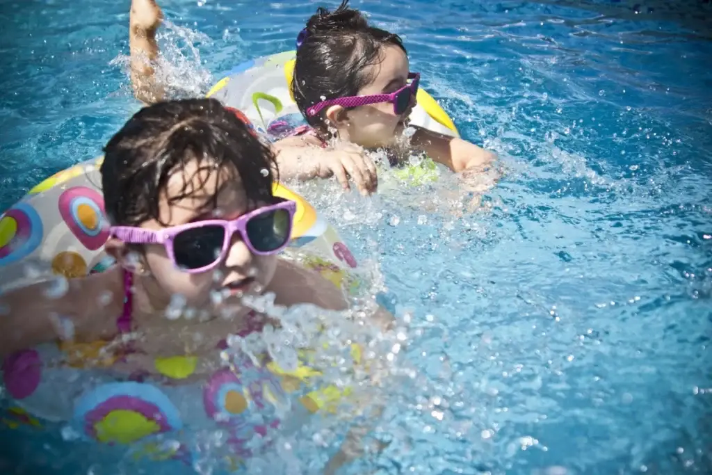 Two kids in colorful swimsuits and sunglasses play with inflatables in a pool serviced by Grey Shark Pool Services, Oak Island, NC.